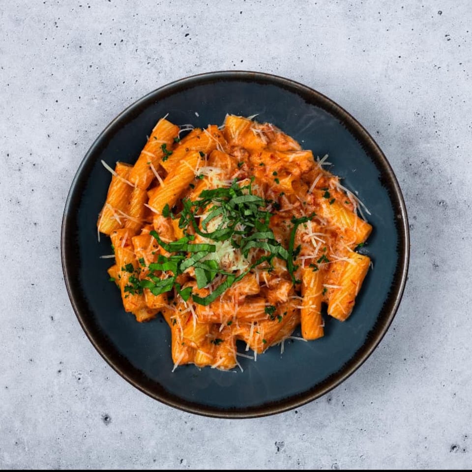Rigatoni pasta in a creamy tomato sauce, topped with fresh basil and grated Parmesan cheese.