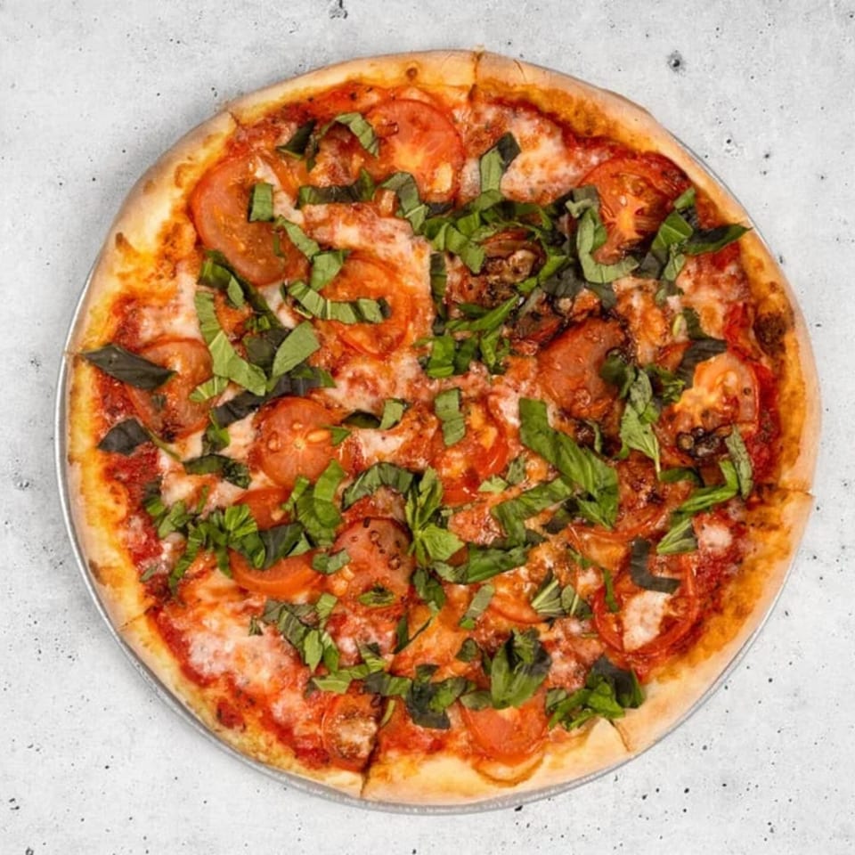 A whole margherita pizza with sliced tomatoes, melted mozzarella, and fresh basil on a light background.