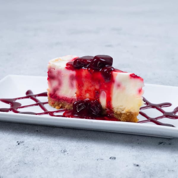 A slice of cheesecake with a graham cracker crust, topped with cherry sauce and whole cherries.