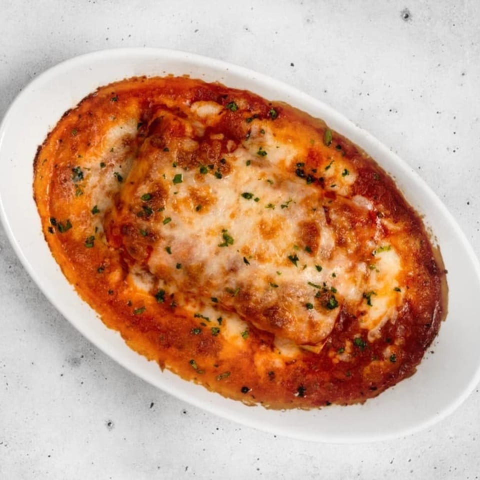 Baked lasagna with melted cheese and herbs in a white oval dish on a light background.
